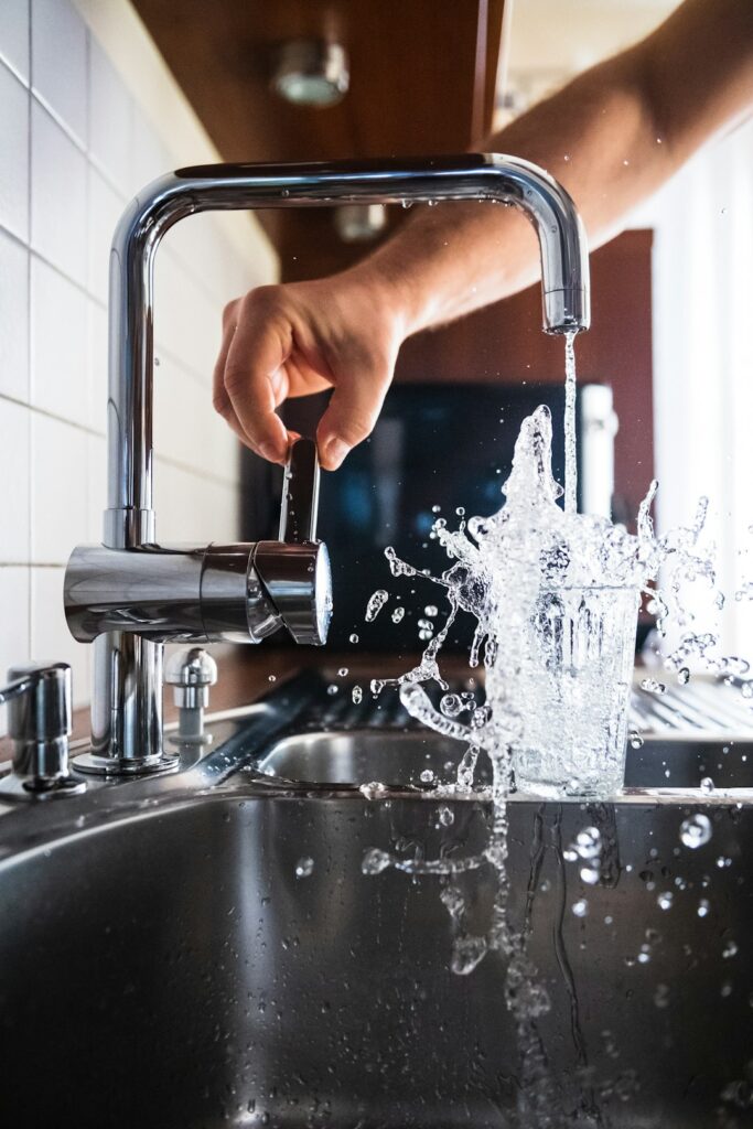 Person using a wrench to repair a bathroom faucet with tools and small parts on the sink edge.