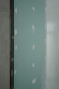 A person smoothing drywall spackle over a small hole with a putty knife on a painted wall.