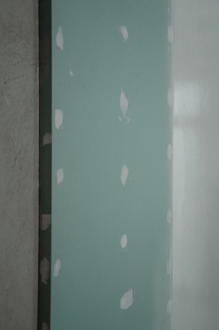 A person smoothing drywall spackle over a small hole with a putty knife on a painted wall.