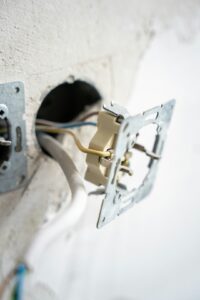 A person using a screwdriver to replace an electrical wall outlet in a residential setting.